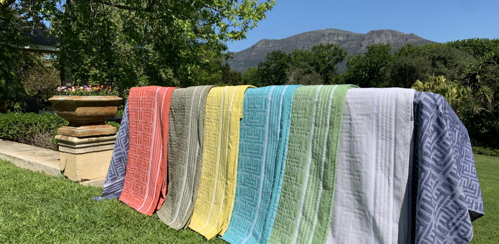 A rainbow of Kuba Cotton throws layed in front of Cape Town Mountain scenary
